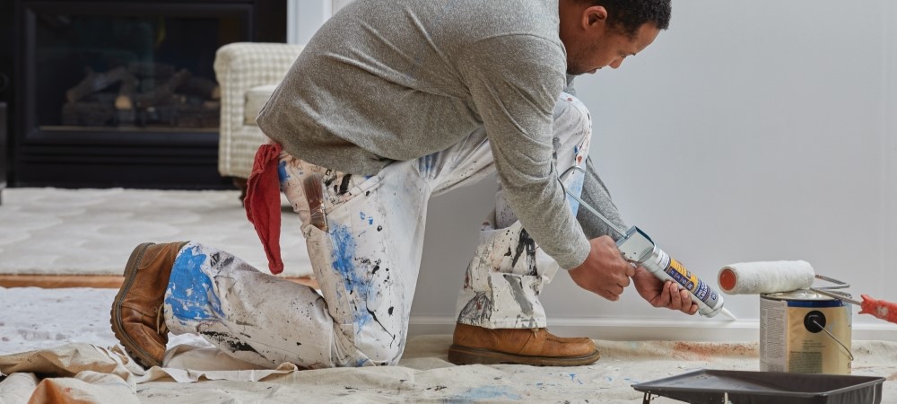 A homeowner applies caulk to baseboards