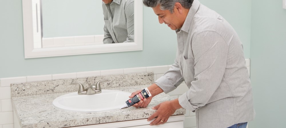 A homeowner applying silicone kitchen and bath sealant to a bathroom sink