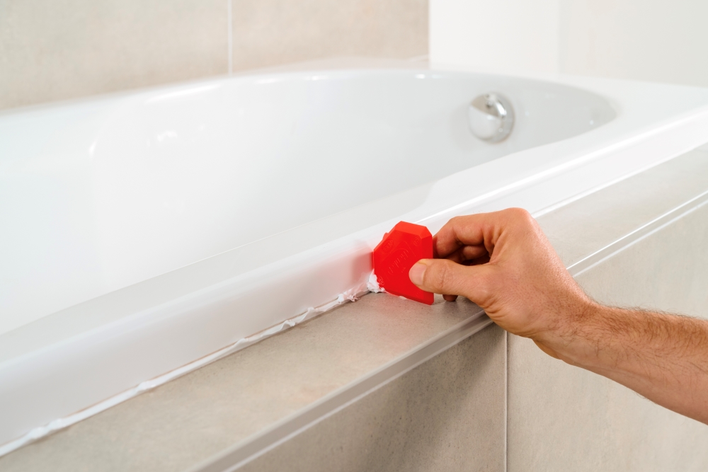 A homeowner wiping off excess sealant from the edges of a bathtub.