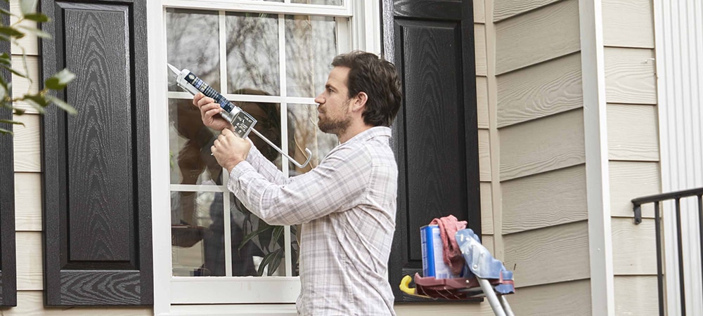 A homeowner sealing windows around the exterior of a home