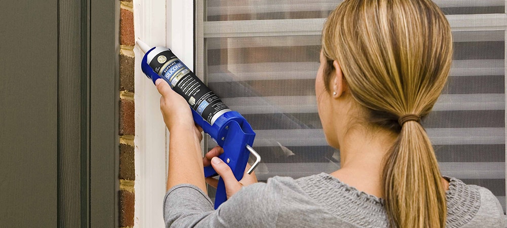 A homeowner applying silicone sealant with a caulking gun.